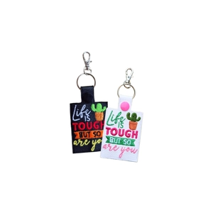 Two faux leather keyrings embroidered with the phrase 'Life Is Tough But So Are You' and a small cactus design. One keyring is black with red, orange, yellow, white and green stitching, and the other is white with pink, green, orange and white stitching. Both have a metal keyring and lobster clasp.