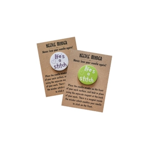 Life’s a Stitch needle minder shown on a kraft backing card, featuring round design with heart detail and text, available in multiple colour options.