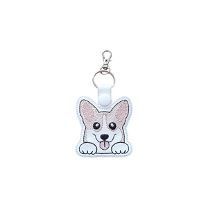 A kawaii-style corgi dog keyring made from faux leather, featuring a cute embroidered corgi face with large upright ears, bright eyes, a tongue-out smile, and little paws, finished with a metal keyring and snap tab.