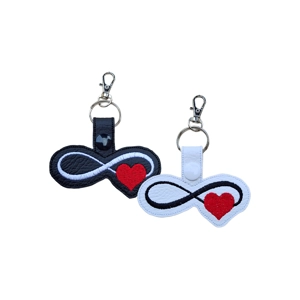 A faux leather infinity heart keyring shown in two colour options, one black and one white, featuring a stitched infinity symbol flowing into a heart.