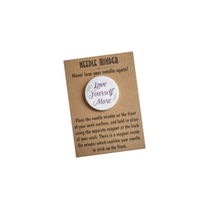 Love Yourself More needle minder shown on a kraft backing card, featuring a round design with text and leaf accents on a white background.