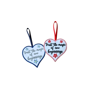 Two heart-shaped decorations with hanging ribbons, each embroidered with the message ‘Trust the magic of new beginnings’. One has a navy blue border with blue and yellow floral details, and the other has a red border with red floral details.