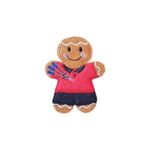 A gingerbread darts character wearing a red top with a black collar and dark trousers, holding a set of blue dart flights, with stitched facial details and a cheerful expression.