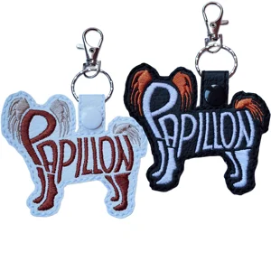 Two Papillon word art dog keyrings in black and white faux leather, with two-colour embroidered breed designs and metal clasp fittings.