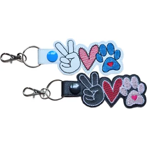 Two Paw Print Peace Love keyrings in black and white faux leather, each featuring a peace sign hand, stitched heart and paw print design with sturdy metal ring and lobster clasp.