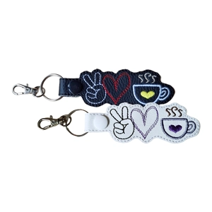 Two Peace Love Coffee keyrings, one in black and one in white. Each faux leather keyring is machine embroidered with a peace sign hand, a stitched heart, and a steaming coffee cup with a small heart on the cup and finished with a metal keyring and clasp.