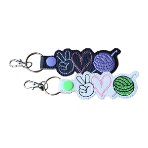 Two Peace Love Crochet keyrings, one black and one white, machine embroidered with a peace sign hand, a stitched heart and a ball of yarn in contrasting colours.