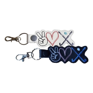 Two embroidered keyrings showing Peace, Love, Hockey. The white keyring has black, red, and grey stitching. The black keyring has white, pink, and blue stitching. Each features a peace hand sign, a heart, and crossed hockey sticks with a puck.