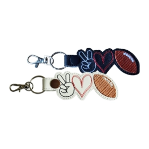 Two embroidered snap-tab keyrings, each shaped around three stitched icons: a peace-sign hand, a heart and a rugby ball. One keyring is made from black faux leather with white, red and brown stitching. The other is made from white faux leather with black, red and brown stitching. Both keyrings have silver hardware.