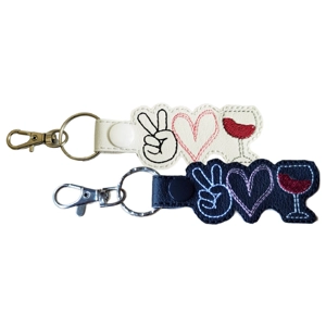 Peace Love Wine embroidered keyrings shown in white and black faux leather, featuring a peace hand symbol, stitched heart and wine glass design, finished with metal rings and lobster clasps.
