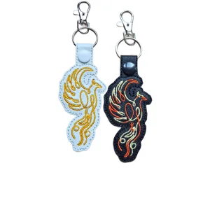 Black and white faux leather phoenix keyrings with embroidered flame style bird designs, shown with silver metal clips and split rings.