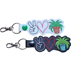 Two Plant Peace Love keyrings in black and white faux leather, each featuring a peace sign hand, stitched heart and potted houseplant design with sturdy metal ring and lobster clasp.