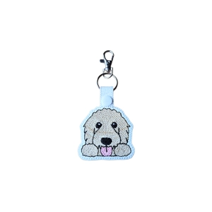 A kawaii-style goldendoodle dog keyring made from faux leather, featuring a playful goldendoodle with fluffy fur, round black eyes, a small black nose, and a pink tongue, finished with a metal keyring and lobster clasp.