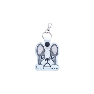 A kawaii-style French Bulldog keyring with a pouty expression, machine embroidered in black and grey thread on white faux leather, with a metal keyring and lobster clasp attached.