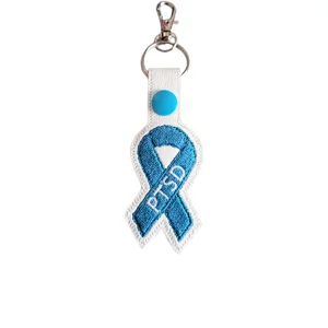 White faux leather PTSD awareness keyring with an embroidered teal ribbon design, finished with a teal snap button and silver metal hardware.