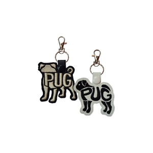 Two Pug-shaped faux leather keyrings, one black with tan embroidery and one white with black embroidery. Each features the word 'PUG' stitched into the design and includes a snap tab, keyring and metal clasp for attaching to keys or bags.