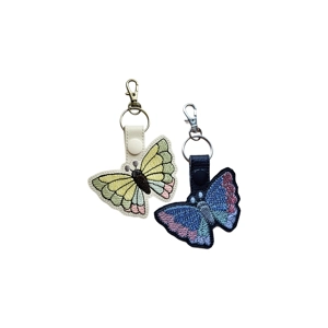 Two butterfly keyrings, one on white faux leather with soft pastel wing segments and one on black faux leather with blue and pink wing segments.