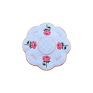 Round embroidered table mat with scalloped edges, pink border, and pink rose motifs around the edge, featuring the word “Rose” and a central stippling pattern.