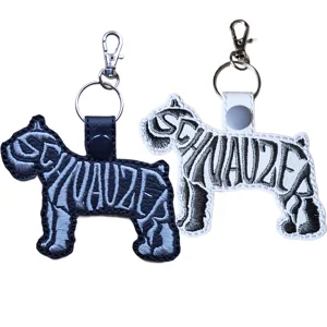 Two Schnauzer word art keyrings shown in black faux leather with grey stitching and white faux leather with black stitching, both finished with metal clasp hardware.