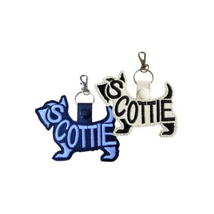 Scottie (Scottish Terrier) word-art keyring shown in black and white faux leather, featuring an embroidered Scottie silhouette with attached metal keyring and clasp, displayed in two colour options.
