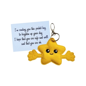 A yellow felt star with a smiling embroidered face and outstretched arms is attached to a silver keyring and clasp. Behind it is a white keepsake card with a handwritten-style message about sending a pocket hug to brighten someone’s day.