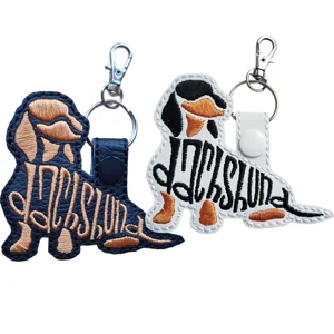 Two sitting Dachshund word art keyrings in black and white faux leather, embroidered with breed lettering and finished with metal keyring clips.