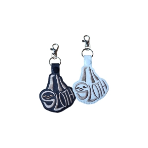 Two embroidered sloth word art keyrings, one in black and one in white, with the word “Sloth” stitched to form the shape of a smiling sloth, each finished with a metal clasp and keyring.