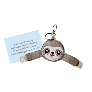 A smiling felt sloth pocket hug with outstretched arms, slightly padded and machine embroidered, attached to a silver keyring clip and shown beside a printed keepsake card.