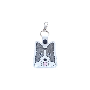 A kawaii-style Border Collie dog keyring made from faux leather, featuring a cute embroidered Border Collie face with alert ears, wide eyes, a small tongue-out smile, and little paws, finished with a metal keyring and snap tab.