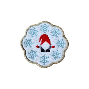 A round embroidered candle coaster featuring a red-hatted gnome at the centre, surrounded by pale blue snowflakes and finished with a scalloped stitched edge.