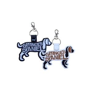 Springer Spaniel word-art keyring shown in black and white faux leather, featuring an embroidered Springer Spaniel silhouette with attached metal keyring and clasp, displayed in two colour options.
