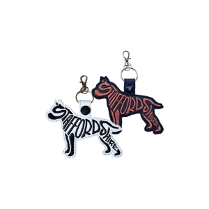 Staffordshire Terrier word-art keyring shown in black and white faux leather, featuring an embroidered Staffordshire Terrier silhouette with attached metal keyring and clasp, displayed in two colour options.