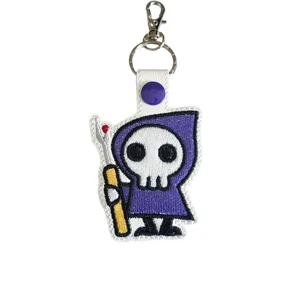Embroidered sewing themed keyring featuring hooded stitch character holding seam ripper made from faux leather with metal clasp and decorative stitching details