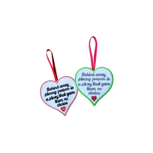Two heart-shaped felt hanging decorations embroidered with the phrase “Behind every strong person is a story that gave them no choice.” One has a red border with black text, a red heart motif, and a red ribbon. The other has a lime green border with grey text, a dark pink heart motif, and a pink ribbon.