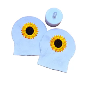 Two white felt sunflower tealight covers with embroidered yellow sunflowers, shown beside a small LED tealight.