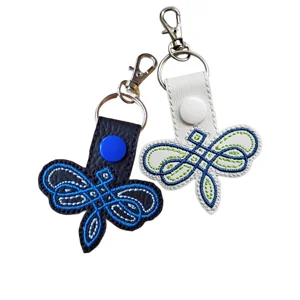 Black and white Celtic dragonfly keyrings with embroidered details, colourful snap buttons and silver metal hardware.