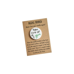 A round white needle minder with the words “Take care of you”, featuring coloured lettering for the word “you” and a small floral detail, displayed on a kraft needle minder backing card with printed instructions.