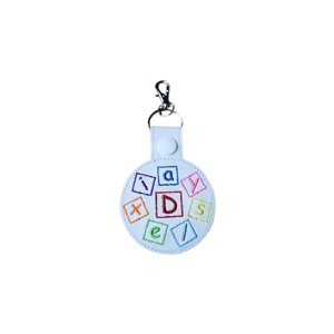 A round faux leather keyring featuring colourful embroidered letter blocks spelling out the word ‘dyslexia’, finished with a metal keyring and lobster clasp.