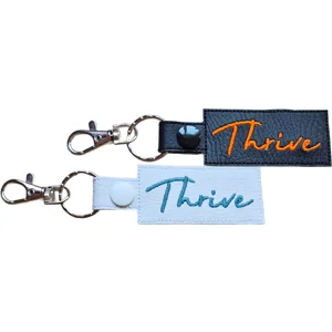 Black and white faux leather Thrive positive word keyrings with embroidered lettering, metal clasps and matching popper fastenings.