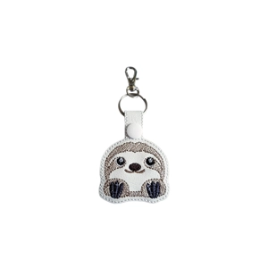 A kawaii sloth keyring on white faux leather with a sleepy, smiling sloth design and a metal clip.