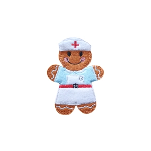 A handmade felt gingerbread character designed as a vintage nurse, featuring a light blue top, white apron with a red belt, and a white nurse’s cap embroidered with a red cross. The smiling gingerbread has pink stitched cheeks and brown felt “icing” details, representing a traditional retro-style nurse uniform.