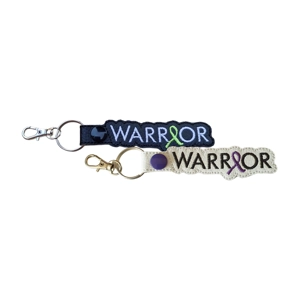 Two Warrior Awareness keyrings, one black with a green awareness ribbon and one white with a purple awareness ribbon, made from faux leather and machine embroidered, each with a metal keyring and clasp.