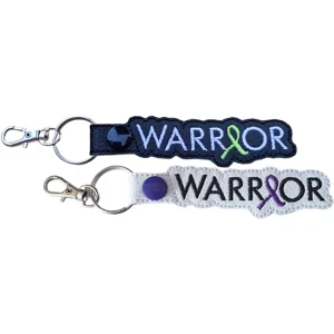 Two Warrior awareness ribbon keyrings shown in black and white faux leather, with embroidered wording, coloured ribbon details and silver keyring hardware.