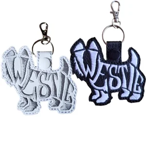 Westie word art keyrings shown in white and black faux leather, with embroidered dog-shaped designs and silver keyring clasps.