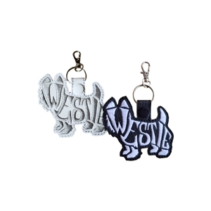 Embroidered West Highland Terrier (Westie) keyring shown in black and white colour options, featuring a word-art dog silhouette with metal keyring and clasp on a white background.