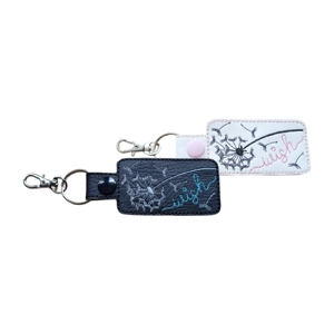 Two faux leather keyrings with embroidered dandelion designs and the word wish. One is black with teal and silver stitching and a black snap, and the other is white with pink and grey stitching and a pink snap. Both have metal keyrings and lobster clasps.