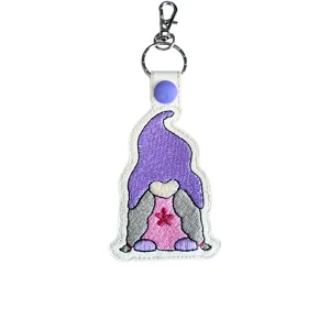 Embroidered faux leather woodland girl gnome keyring with purple hat, pink dress, grey hair and flower detail, attached to a metal clasp and ring.