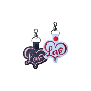 Two heart-shaped keyrings embroidered with the word ‘Love’ in a script design, made from faux leather with metal keyring fittings.