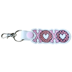 A faux leather XOXO keyring featuring embroidered letters in pink with heart details, finished with a metal keyring and lobster clasp attachment.