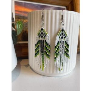 Handmade beaded earrings in shades of green and white, featuring an intricate geometric pattern and long fringe design. The earrings hang from silver hooks and are displayed against a textured white ceramic background